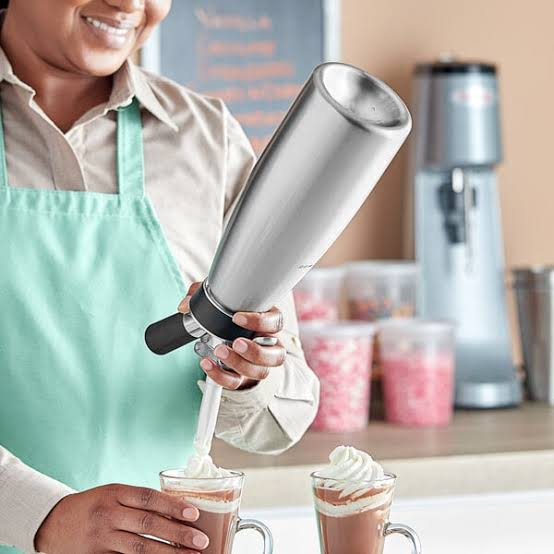 Barista using the QuickWhip PRO 1L cream dispenser to top hot drinks with fresh whipped cream